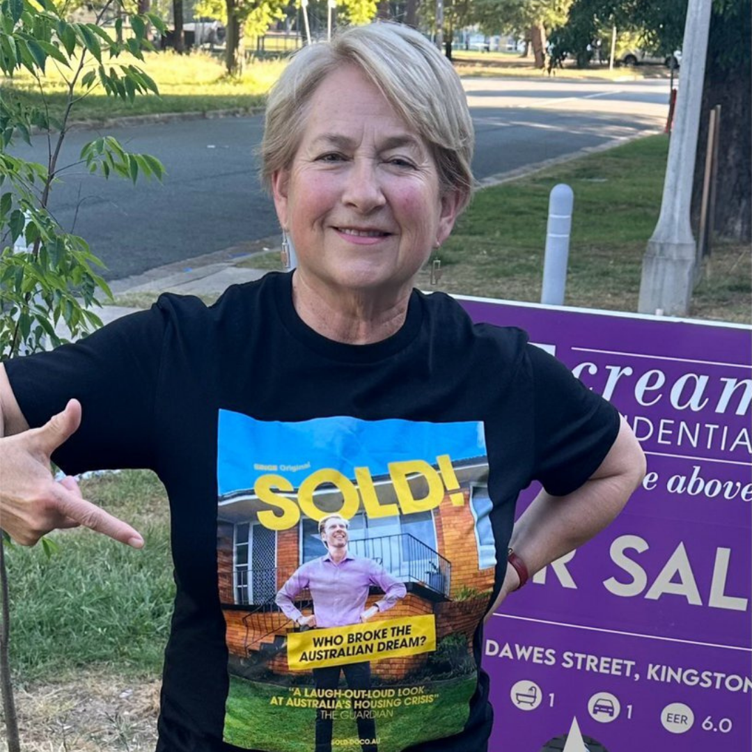 Barbara Pocock smiling and pointing to t-shirt that reads 'who broke the Australian dream'