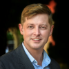 This is an image of Paul, a smiling individual with brown hair and a blue collared shirt, and a blazer on top.