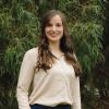 This is a photo of Jill, who is standing outside in a parkland environment. She is wearing a cream coloured shirt and her dark brown hair falls below her shoulders. She's smiling warmly at the camera.