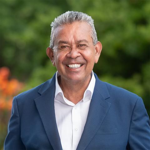 Profile picture of Greens Candidate Uncle James Williams. Uncle James is wearing a blue suit and is standing in front of blurred out greenery