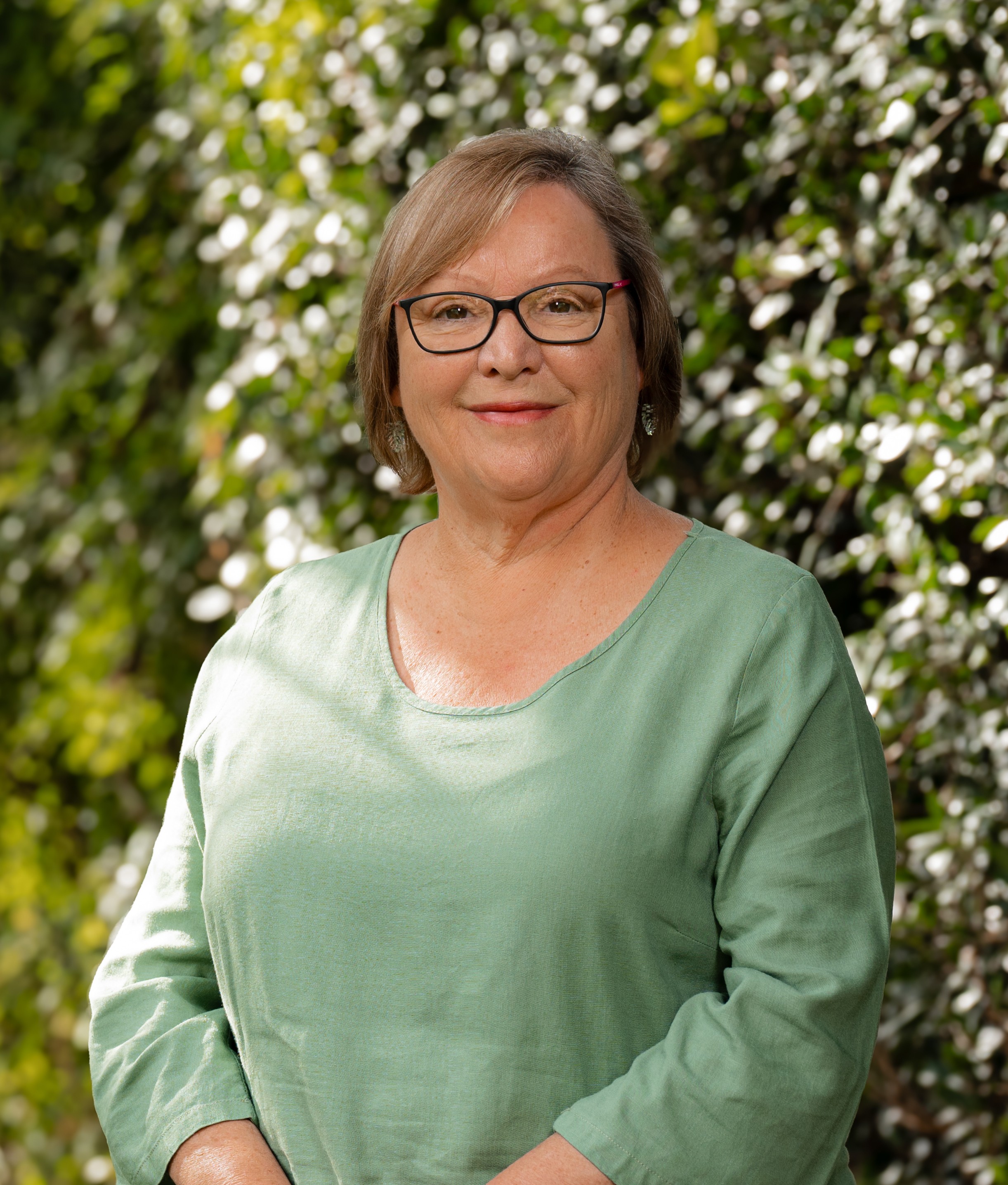Bev Morris in front of a green leafy background