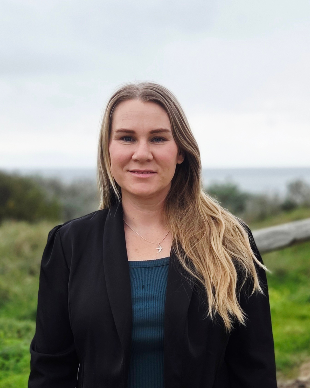 Rhi Davies, Greens candidate for the 2026 Secret Harbour by-election, smiling and looking at the camera, with the foreshore in the background.