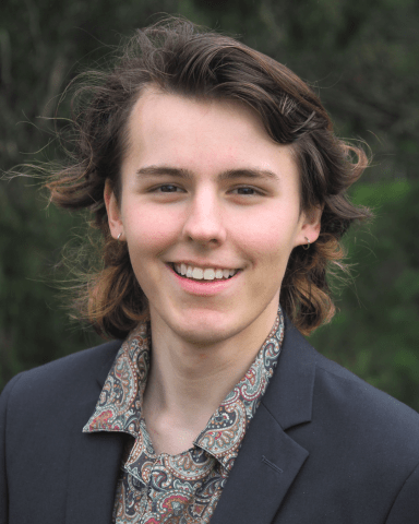 Profile picture of Logan Farrell, Greens candidate for Beale ward by-election. Logan is standing in front of blurred out leaveless tree and is wearing a patterned shirt with a black blazer